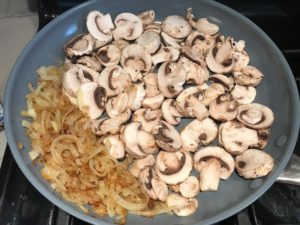 Sliced onions cooked on one side of skillet and raw mushroom slices in the other half for the Caramelized Onions & Mushrooms on Pork Tenderloin recipe. This is such a flavorful main dish! The pork tenderloin is moist and juicy and topped with Onions & Mushrooms that are sauteed low and slow with a touch of balsamic to bring out all of the natural sugars and caramelize them to perfection.
