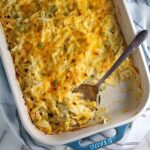 Golden brown cheesy Hash Brown Casserole without Soup in a Staub Casserole dish on counter with a rustic serving spoon in the corner where some casserole has been taken out.