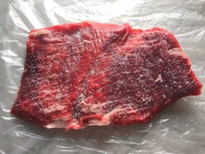 Raw flank steak with salt added to prep it for the Stuffed Flank Steak recipe. it is oozing with flavor! First, you get mushrooms, onions, and garlic sauteed together. Then they are mixed with fresh parsley and basil, then parmesan, and goat cheese! Roll it all up in Flank Steak and roast for an amazing dinner.