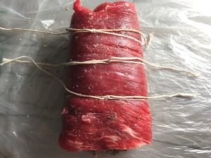 Raw flank steak rolled and tied with Mushroom stuffing inside. This Stuffed Flank Steak recipe is oozing with flavor! First, you get mushrooms, onions, and garlic sauteed together. Then they are mixed with fresh parsley and basil, then parmesan, and goat cheese! Roll it all up in Flank Steak and roast for an amazing dinner.