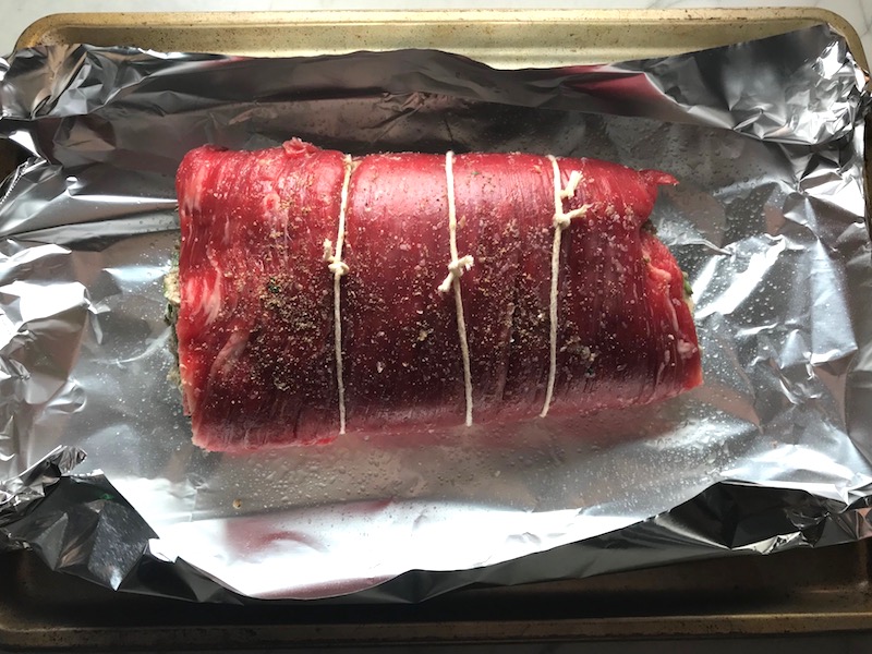 Raw flank steak rolled and tied with Mushroom stuffing inside. This Stuffed Flank Steak recipe is oozing with flavor! First, you get mushrooms, onions, and garlic sauteed together. Then they are mixed with fresh parsley and basil, then parmesan, and goat cheese! Roll it all up in Flank Steak and roast for an amazing dinner.