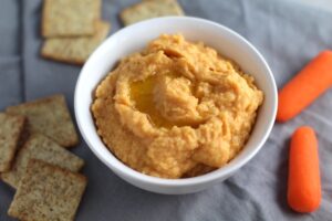2-Ingredient Magical Sriracha Hummus in a bowl with crackers and carrots next to it. This is seriously the easiest hummus you will ever make and it's perfect for snacking or adding to a meal. The chickpeas have so much flavor and the Sriracha gives it a kick that is totally addictive!
