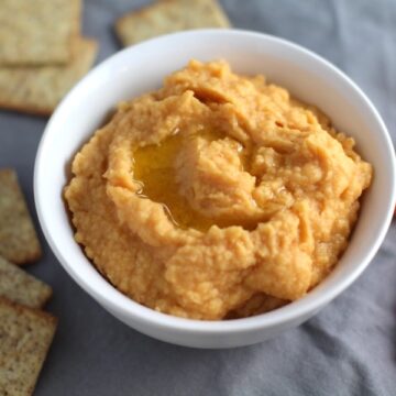 2-Ingredient Magical Sriracha Hummus in a bowl with crackers and carrots next to it. This is seriously the easiest hummus you will ever make and it's perfect for snacking or adding to a meal. The chickpeas have so much flavor and the Sriracha gives it a kick that is totally addictive!