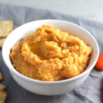 2-Ingredient Magical Sriracha Hummus in a bowl with crackers and carrots next to it. This is seriously the easiest hummus you will ever make and it's perfect for snacking or adding to a meal. The chickpeas have so much flavor and the Sriracha gives it a kick that is totally addictive!
