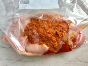 Sun Dried Tomato sauce in bag with raw chicken. Sun Dried Tomato Chicken is slightly sweet, slightly tart and tangy, and hugely delicious! When Sun dried tomatoes are rehydrated and blended, they turn into a thick and lucious sauce that coats the chicken keeping it moist and juicy when it simply bakes in the oven. It's a perfect easy weeknight dinner that you can prepare ahead and cook quickly! #chicken #chickenrecipes #easydinners #dinnerrecipes