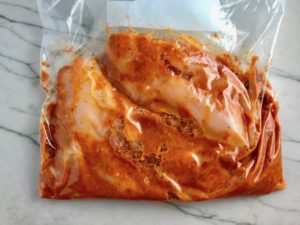 Sun Dried Tomato sauce in bag with raw chicken. Sun Dried Tomato Chicken is slightly sweet, slightly tart and tangy, and hugely delicious! When Sun dried tomatoes are rehydrated and blended, they turn into a thick and lucious sauce that coats the chicken keeping it moist and juicy when it simply bakes in the oven. It's a perfect easy weeknight dinner that you can prepare ahead and cook quickly! #chicken #chickenrecipes #easydinners #dinnerrecipes