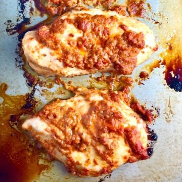 Sun Dried Tomato Chicken breasts cooked on a pan. It's slightly sweet, slightly tart and tangy, and hugely delicious! When Sun dried tomatoes are rehydrated and blended, they turn into a thick and lucious sauce that coats the chicken keeping it moist and juicy when it simply bakes in the oven. It's a perfect easy weeknight dinner that you can prepare ahead and cook quickly! #chicken #chickenrecipes #easydinners #dinnerrecipes