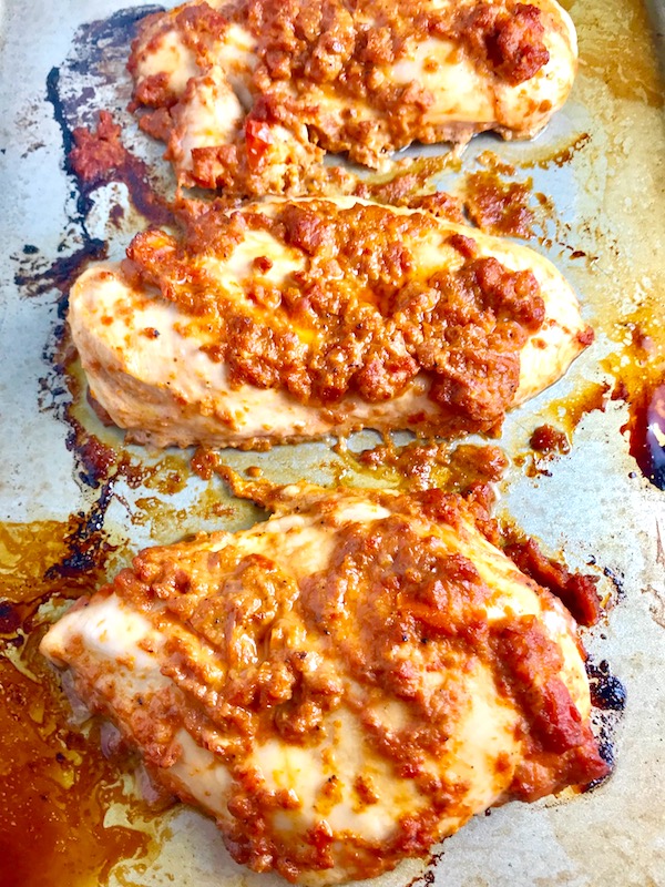 Sun Dried Tomato Chicken breasts cooked on a pan. It's slightly sweet, slightly tart and tangy, and hugely delicious! When Sun dried tomatoes are rehydrated and blended, they turn into a thick and lucious sauce that coats the chicken keeping it moist and juicy when it simply bakes in the oven. It's a perfect easy weeknight dinner that you can prepare ahead and cook quickly! #chicken #chickenrecipes #easydinners #dinnerrecipes