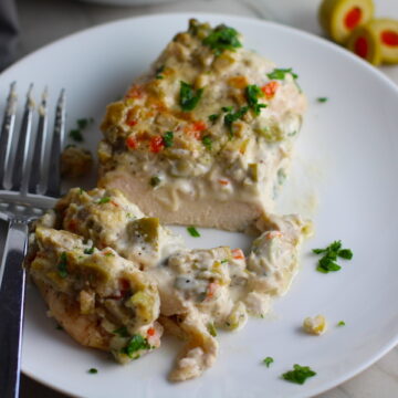 Creamy Olive Chicken cut on plate with fork. This is magnificently thick and creamy and infused with garlic flavor and nuttiness from the Parmesan. The best part; however, is the salty and briny flavor kick from the green olives with a little sweetness from the pimiento. #chicken #chickenrecipes #chickendinner #easydinners #easyrecipes #comfortfood #casserole