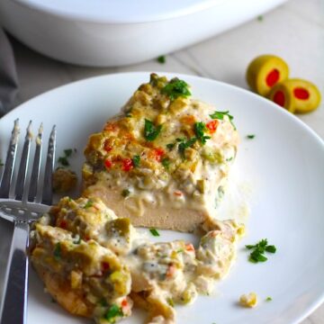 Creamy Olive Chicken cut on plate with fork and casserole dish in background. This is magnificently thick and creamy and infused with garlic flavor and nuttiness from the Parmesan. The best part; however, is the salty and briny flavor kick from the green olives with a little sweetness from the pimiento. #chicken #chickenrecipes #chickendinner #easydinners #easyrecipes #comfortfood #casserole