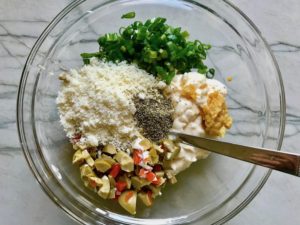 Chopped green olives and pimiento, mayo, garlic, scallion, parmesan, and pepper in bowl for the Creamy Olive Chicken recipe. This is magnificently thick and creamy and infused with garlic flavor and nuttiness from the Parmesan. The best part; however, is the salty and briny flavor kick from the green olives with a little sweetness from the pimiento. #chicken #chickenrecipes #chickendinner #easydinners #easyrecipes #comfortfood #casserole