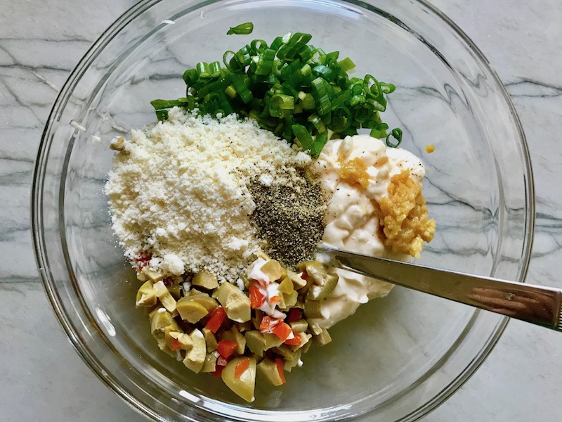 Chopped green olives and pimiento, mayo, garlic, scallion, parmesan, and pepper in bowl for the Creamy Olive Chicken recipe. This is magnificently thick and creamy and infused with garlic flavor and nuttiness from the Parmesan. The best part; however, is the salty and briny flavor kick from the green olives with a little sweetness from the pimiento. #chicken #chickenrecipes #chickendinner #easydinners #easyrecipes #comfortfood #casserole