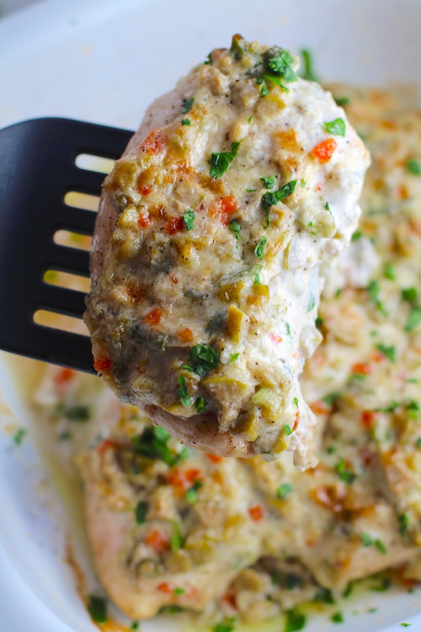 Spatula lifting Creamy Olive Chicken from a casserole dish. This is magnificently thick and creamy and infused with garlic flavor and nuttiness from the Parmesan. The best part; however, is the salty and briny flavor kick from the green olives with a little sweetness from the pimiento. #chicken #chickenrecipes #chickendinner #easydinners #easyrecipes #comfortfood #casserole