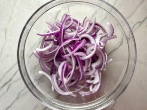Red Onions in bowl before pickling for Slow Cooker Pork Tacos with with Pickled Onions, Shredded Cheese, and Cilantro Lime Crema drizzled on top! It's such an easy dinner since the pork cooks in the slow cooker to be perfectly seasoned and fall apart tender. #tacos #easydinner #glutenfree #dinner #mexican #pork