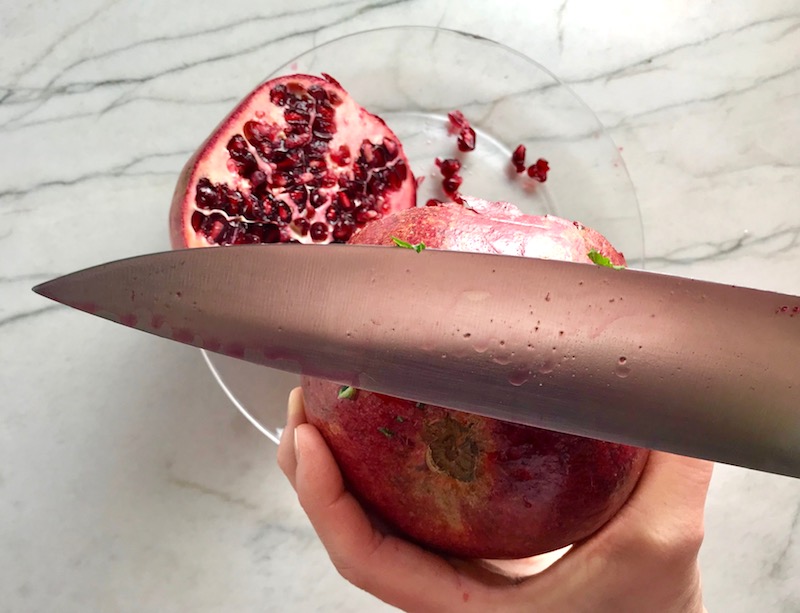 Knife hitting Pomegranate to get seeds out for Quinoa & Kale Salad with Roasted Chickpeas, Pomegranate, Feta, red pepper, and Creamy Lemon Dressing. #glutenfree #lunch #dinner #healthyrecipes #healthyfood #salads #quinoa #kale