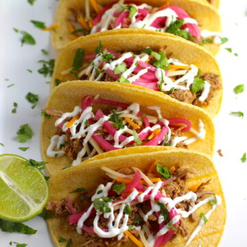 Slow Cooker Pork Tacos with with Pickled Onions, Shredded Cheese, and Cilantro Lime Crema drizzled on top! It's such an easy dinner since the pork cooks in the slow cooker to be perfectly seasoned and fall apart tender. #tacos #easydinner #glutenfree #dinner #mexican #pork