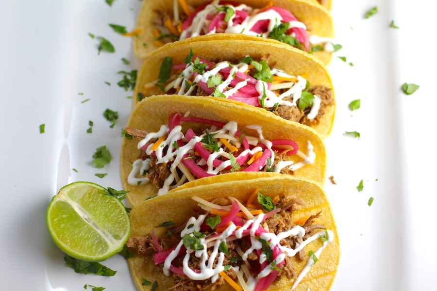Slow Cooker Pork Tacos with with Pickled Onions, Shredded Cheese, and Cilantro Lime Crema drizzled on top! It's such an easy dinner since the pork cooks in the slow cooker to be perfectly seasoned and fall apart tender. #tacos #easydinner #glutenfree #dinner #mexican #pork