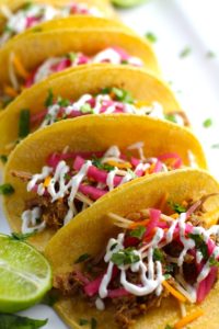 Slow Cooker Pork Tacos with with Pickled Onions, Shredded Cheese, and Cilantro Lime Crema drizzled on top! It's such an easy dinner since the pork cooks in the slow cooker to be perfectly seasoned and fall apart tender. #tacos #easydinner #glutenfree #dinner #mexican #pork