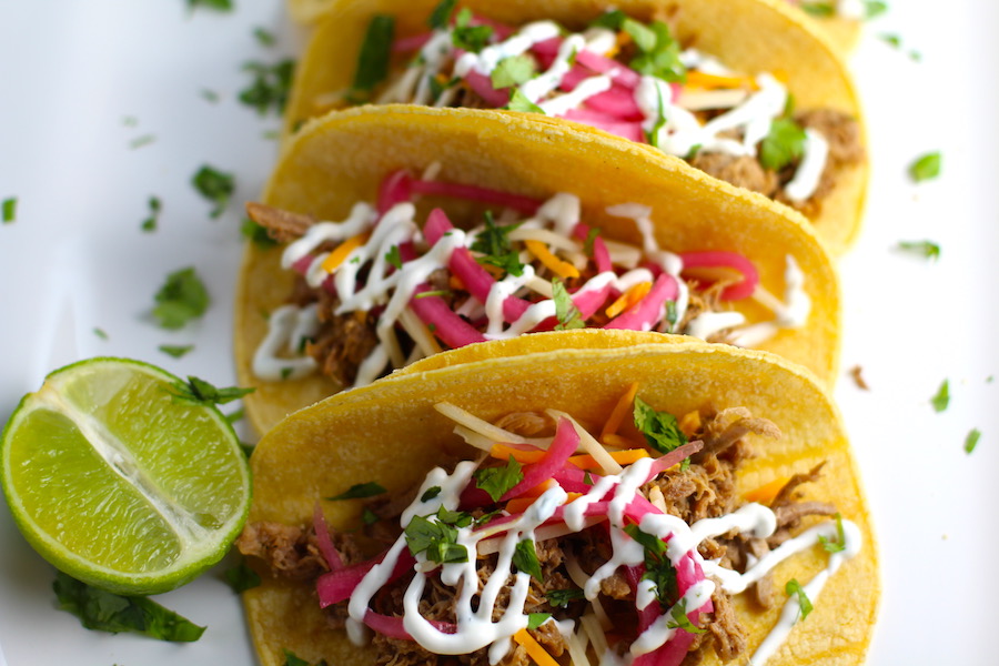 Slow Cooker Pork Tacos with with Pickled Onions, Shredded Cheese, and Cilantro Lime Crema drizzled on top! It's such an easy dinner since the pork cooks in the slow cooker to be perfectly seasoned and fall apart tender. #tacos #easydinner #glutenfree #dinner #mexican #pork