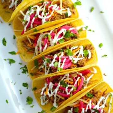 Slow Cooker Pork Tacos with with Pickled Onions, Shredded Cheese, and Cilantro Lime Crema drizzled on top!  It's such an easy dinner since the pork cooks in the slow cooker to be perfectly seasoned and fall apart tender. #tacos #easydinner #glutenfree #dinner #mexican #pork