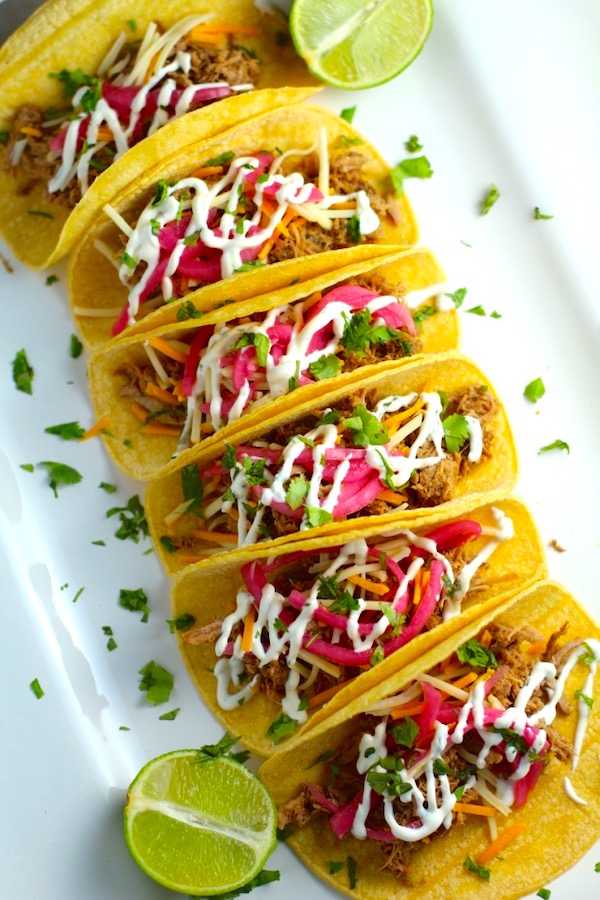 Slow Cooker Pork Tacos with with Pickled Onions, Shredded Cheese, and Cilantro Lime Crema drizzled on top! It's such an easy dinner since the pork cooks in the slow cooker to be perfectly seasoned and fall apart tender. #tacos #easydinner #glutenfree #dinner #mexican #pork