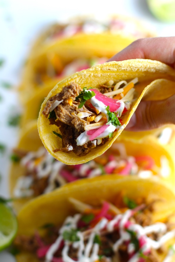 Hand holding a Slow Cooker Pork Taco with with Pickled Onions, Shredded Cheese, and Cilantro Lime Crema drizzled on top! It's such an easy dinner since the pork cooks in the slow cooker to be perfectly seasoned and fall apart tender. #tacos #easydinner #glutenfree #dinner #mexican #pork