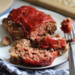 5-Ingredient Chipotle Meatloaf sliced on white plate. This recipe adds a spicy mexican flare with Chipotle Peppers in Adobo Sauce and Cheddar Cheese.  It's incredibly easy, incredibly moist, and incredibly delicious!  A family dinner favorite! #meatloaf #mexican #easydinner #familydinner #dinner #easyrecipes #beef