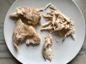 Shredding roasted chicken on a plate for Curry Chicken Salad. It has so many fantastic flavors and textures! The chicken breast is simply roasted and mixed with a creamy sweet and savory curry dressing. Red pepper gives you a fresh crunch, scallion gives a savory bite, and raisins give a burst of sweet. #chicken #chickenrecipes #chickensalad #currychicken #mealprep #lunch #healthyrecipes