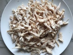 Shredded chicken on a plate for Curry Chicken Salad. It has so many fantastic flavors and textures! The chicken breast is simply roasted and mixed with a creamy sweet and savory curry dressing. Red pepper gives you a fresh crunch, scallion gives a savory bite, and raisins give a burst of sweet. #chicken #chickenrecipes #chickensalad #currychicken #mealprep #lunch #healthyrecipes