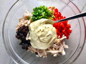 Curry Dressing, shredded chicken, red pepper, scallion, and raisins in bowl for Curry Chicken Salad. It has so many fantastic flavors and textures! The chicken breast is simply roasted and mixed with a creamy sweet and savory curry dressing. Red pepper gives you a fresh crunch, scallion gives a savory bite, and raisins give a burst of sweet. #chicken #chickenrecipes #chickensalad #currychicken #mealprep #lunch #healthyrecipes