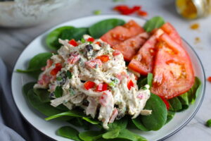 Curry Chicken Salad on spinach with tomato slices. It has so many fantastic flavors and textures! The chicken breast is simply roasted and mixed with a creamy sweet and savory curry dressing. Red pepper gives you a fresh crunch, scallion gives a savory bite, and raisins give a burst of sweet. #chicken #chickenrecipes #chickensalad #currychicken #mealprep #lunch #healthyrecipes
