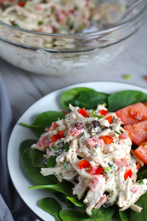 Curry Chicken Salad on spinach with tomato slices. It has so many fantastic flavors and textures! The chicken breast is simply roasted and mixed with a creamy sweet and savory curry dressing. Red pepper gives you a fresh crunch, scallion gives a savory bite, and raisins give a burst of sweet. #chicken #chickenrecipes #chickensalad #currychicken #mealprep #lunch #healthyrecipes