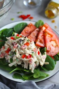Curry Chicken Salad on spinach with tomato slices. It has so many fantastic flavors and textures! The chicken breast is simply roasted and mixed with a creamy sweet and savory curry dressing. Red pepper gives you a fresh crunch, scallion gives a savory bite, and raisins give a burst of sweet. #chicken #chickenrecipes #chickensalad #currychicken #mealprep #lunch #healthyrecipes
