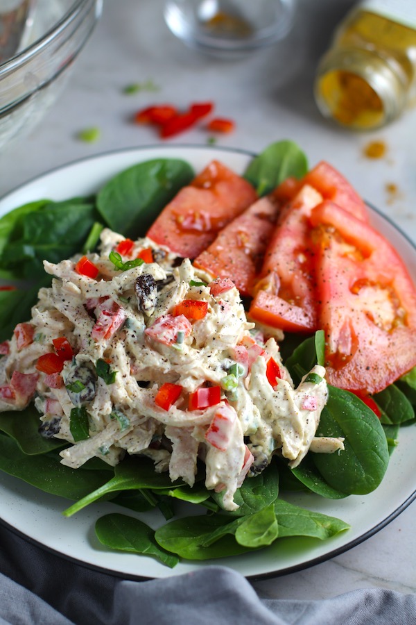 Curry Chicken Salad on spinach with tomato slices. It has so many fantastic flavors and textures! The chicken breast is simply roasted and mixed with a creamy sweet and savory curry dressing. Red pepper gives you a fresh crunch, scallion gives a savory bite, and raisins give a burst of sweet. #chicken #chickenrecipes #chickensalad #currychicken #mealprep #lunch #healthyrecipes