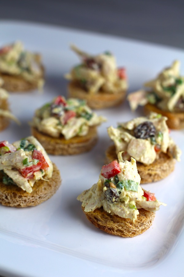 Curry Chicken Salad on toast rouds on plate. It has so many fantastic flavors and textures! The chicken breast is simply roasted and mixed with a creamy sweet and savory curry dressing. Red pepper gives you a fresh crunch, scallion gives a savory bite, and raisins give a burst of sweet. #chicken #chickenrecipes #chickensalad #currychicken #mealprep #lunch #healthyrecipes