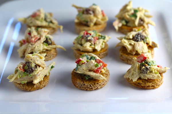 Curry Chicken Salad on toast rouds on plate. It has so many fantastic flavors and textures! The chicken breast is simply roasted and mixed with a creamy sweet and savory curry dressing. Red pepper gives you a fresh crunch, scallion gives a savory bite, and raisins give a burst of sweet. #chicken #chickenrecipes #chickensalad #currychicken #mealprep #lunch #healthyrecipes