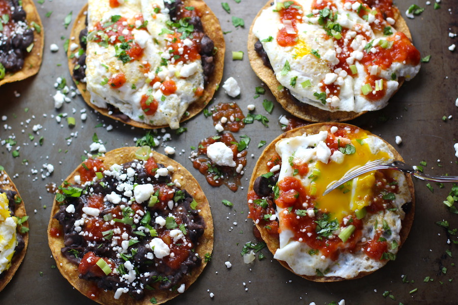 Huevos Tostadas assembled on a sheet pan are utterly delicious! They are similar to the better known Huevos Rancheros but are a pick up and eat with your hands version! They have crispy corn tortillas topped with creamy mashed black beans, a salty fried egg, smoky tomato sauce, cheese, and scallions! #huevosrancheros #eggs #brunch #mexicanrecipes #vegetarian #meatlessrecipes #glutenfree