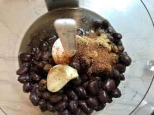 Black Beans, garlic, seasonings in food processor for Huevos Tostadas! They are similar to Huevos Rancheros but are a pick up and eat with your hands version! They have crispy corn tortillas topped with creamy mashed black beans, a salty fried egg, smoky tomato sauce, cheese, and scallions! #huevosrancheros #eggs #brunch #mexicanrecipes #vegetarian #meatlessrecipes #glutenfree