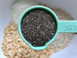 Measuring cup with chia seeds over bowl for No Bake Energy Bites. These Easy Nut-Free, No-Bake Energy Bites with Chocolate Chips are magnificent! They are sweet, chewy, crunchy, & healthy. Only minutes to make & no Baking! Breakfast, snack, or dessert. #energybars #granolabars #snackrecipes #healthyfood #healthyrecipes #healthysnacks #healthybreakfast #healthydessert