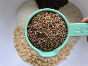 Measuring cup with flaxseed meal over bowl for No Bake Energy Bites. These Easy Nut-Free, No-Bake Energy Bites with Chocolate Chips are magnificent! They are sweet, chewy, crunchy, & healthy. Only minutes to make & no Baking! Breakfast, snack, or dessert. #energybars #granolabars #snackrecipes #healthyfood #healthyrecipes #healthysnacks #healthybreakfast #healthydessert