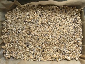 Energy Bite mixture pressed down into parchment lined pan for No Bake Energy Bites. These Easy Nut-Free, No-Bake Energy Bites with Chocolate Chips are magnificent! They are sweet, chewy, crunchy, & healthy. Only minutes to make & no Baking! Breakfast, snack, or dessert. #energybars #granolabars #snackrecipes #healthyfood #healthyrecipes #healthysnacks #healthybreakfast #healthydessert