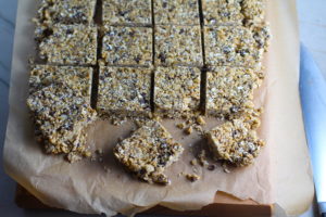 No Bake Energy Bites on parchment and cut into squares. These Easy Nut-Free, No-Bake Energy Bites with Chocolate Chips are magnificent! They are sweet, chewy, crunchy, & healthy. Only minutes to make & no Baking! Breakfast, snack, or dessert. #energybars #granolabars #snackrecipes #healthyfood #healthyrecipes #healthysnacks #healthybreakfast #healthydessert
