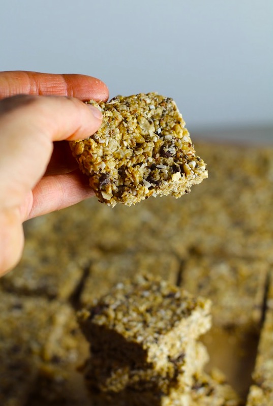 No Bake Energy Bites cut into squares with hand holding one. These Easy Nut-Free, No-Bake Energy Bites with Chocolate Chips are magnificent! They are sweet, chewy, crunchy, & healthy. Only minutes to make & no Baking! Breakfast, snack, or dessert. #energybars #granolabars #snackrecipes #healthyfood #healthyrecipes #healthysnacks #healthybreakfast #healthydessert