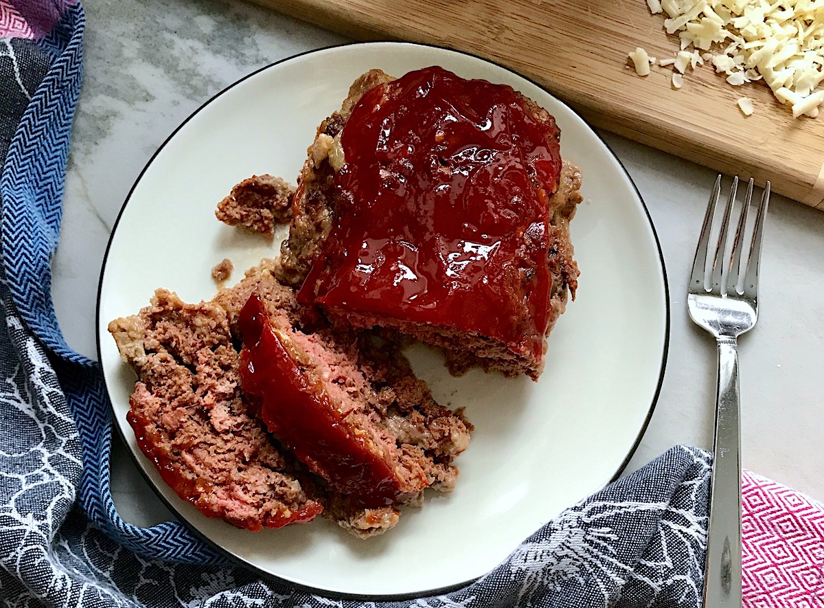 Taco Meatloaf sliced on white plate. This recipe adds a spicy mexican flare with Chipotle Peppers in Adobo Sauce and Cheddar Cheese. It's incredibly easy, incredibly moist, and incredibly delicious! A family dinner favorite!