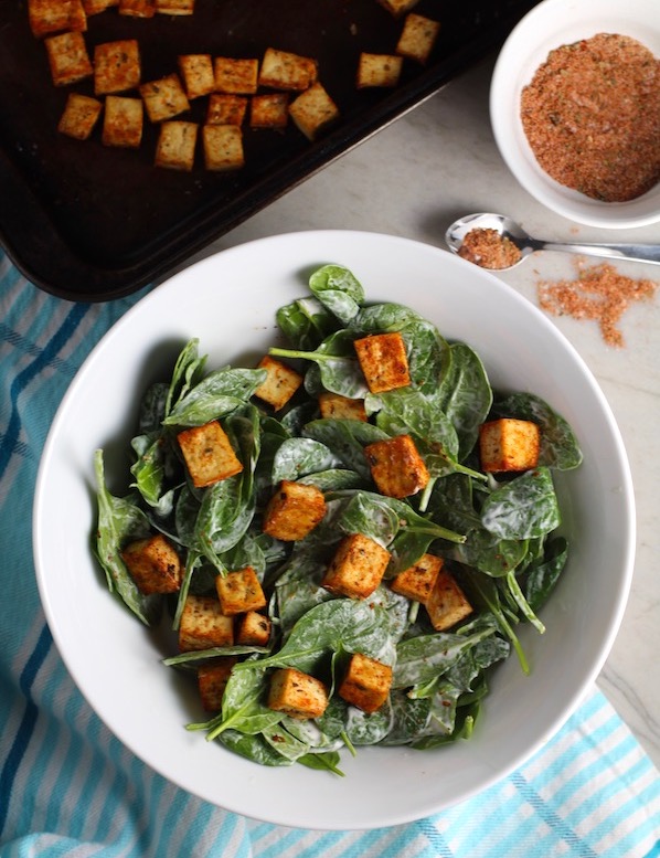 Roasted Tofu Croutons on spinach salad in bowl with croutons on pan in background. These are seasoned and toasted for the perfect addition to any salad, pasta, rice, or soup! They get a roasted, almost nutty flavor with a salty and smoky seasoned crust with a chewy bite. Super easy to make, low carb and great source of protein! #croutons #salad #tofu #tofurecipes #vegetarian #plantbased #paleo