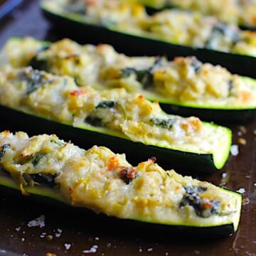 Close up of Artichoke Spinach Stuffed Zucchini Recipe on a pan. Each fantastic bite gives you creamy artichoke, nutty cheesy Parmesan, spinach, and zucchini. Prepare entirely ahead, then bake 20 minutes and enjoy!