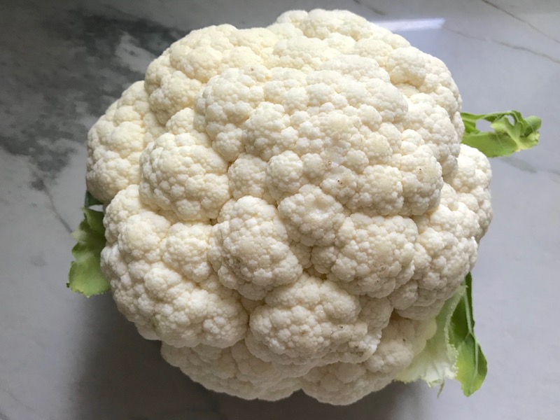 Head of cauliflower for Cauliflower Cordon Bleu Bake recipe. It layers in nutty and salty Gruyere Cheese, with a creamy Vegetable broth based sauce with garlic and parsley. Then the ham and cauliflower are folded into all of this goodness and it's baked in the oven until it all becomes one knock-your-socks-off dish! #cauliflower #lowcarb #glutenfree #casserole #onepot #familydinner #mealprep #easydinner #dinner #healthydinner #healthyfood #healthyrecipes