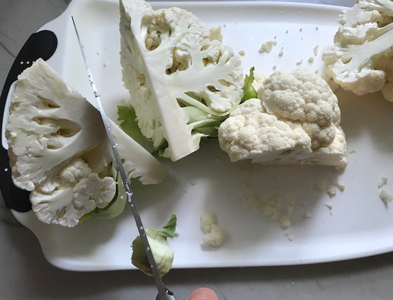 Knife cutting cauliflower for Cauliflower Cordon Bleu Bake recipe. It layers in nutty and salty Gruyere Cheese, with a creamy Vegetable broth based sauce with garlic and parsley. Then the ham and cauliflower are folded into all of this goodness and it's baked in the oven until it all becomes one knock-your-socks-off dish! #cauliflower #lowcarb #glutenfree #casserole #onepot #familydinner #mealprep #easydinner #dinner #healthydinner #healthyfood #healthyrecipes