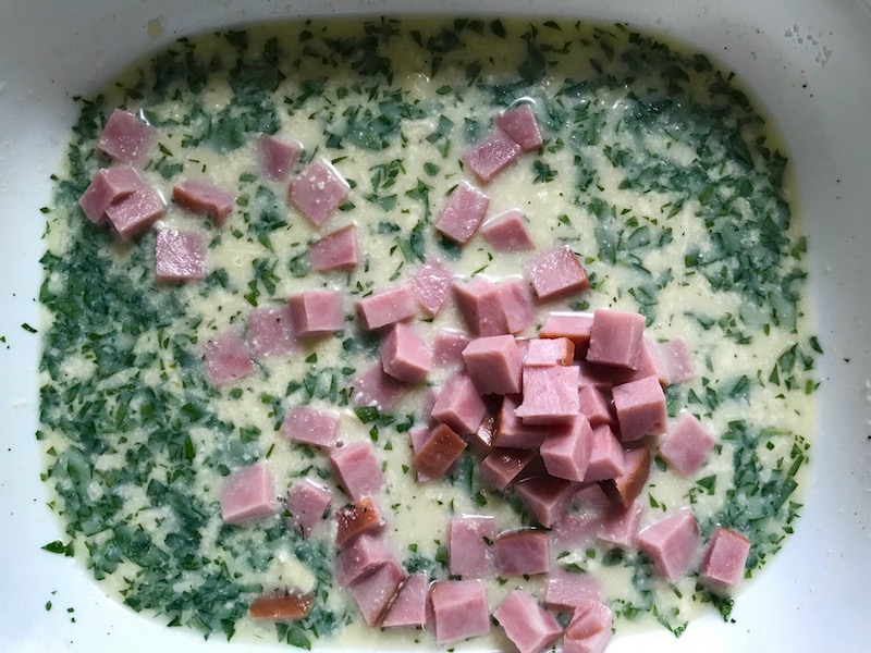 Diced Ham, parsley, and sauce in dish for Cauliflower Cordon Cheese and Ham recipe. It layers in nutty and salty Gruyere Cheese, with a creamy Vegetable broth based sauce with garlic and parsley. Then the ham and cauliflower are folded into all of this goodness and it's baked in the oven until it all becomes one knock-your-socks-off dish! #cauliflower #lowcarb #glutenfree #casserole #onepot #familydinner #mealprep #easydinner #dinner #healthydinner #healthyfood #healthyrecipes