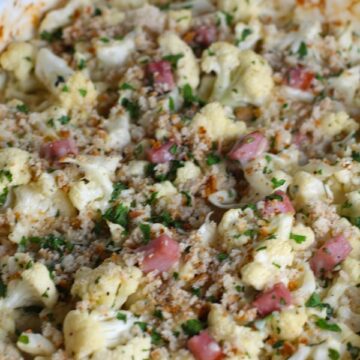 Close up of Cauliflower Cordon Bleu Bake with parsley and breadcrumb topping. It layers in nutty and salty Gruyere Cheese, with a creamy Vegetable broth based sauce with garlic and parsley.  Then the ham and cauliflower are folded into all of this goodness and it's baked in the oven until it all becomes one knock-your-socks-off dish! #cauliflower #lowcarb #glutenfree #casserole #onepot #familydinner #mealprep #easydinner #dinner #healthydinner #healthyfood #healthyrecipes